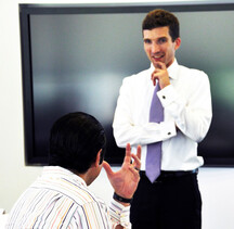 daniel post senning stands at the front of a training classroom and listens to a student asking a question