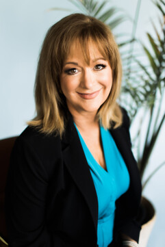 Smiling woman in a blue shirt and black blazer looks at the camera