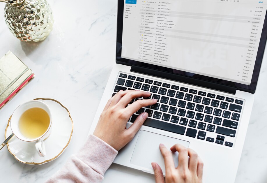 photo of womans hands typing on laptop open to gmail with a cup of tea just to the side