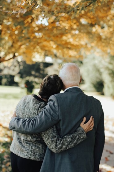 photo: two people with backs turned have their arms around each other and are leaning together with there heads touching