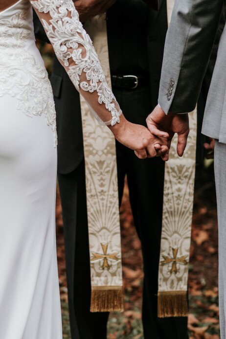 close up photo of couple holding hands in front of a priest