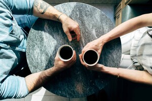 Overhead view of man and woman sitting at a coffee table, uneasily holding their coffee cups