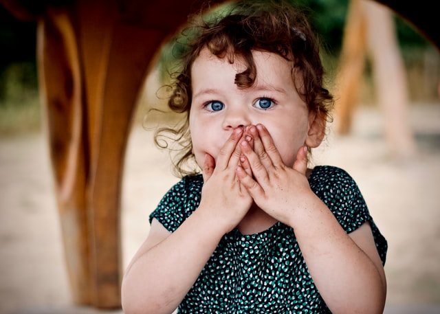 photo: little girl covers her mouth with the oops gesture