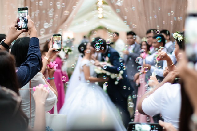 photo: bride and groom kiss amid bubbles while guest hold cell phones and take pictures