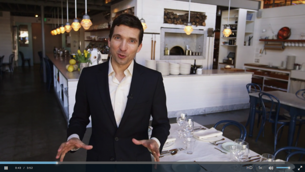 photo: daniel post senning standing in front a set table in a restaurant addressing the camers