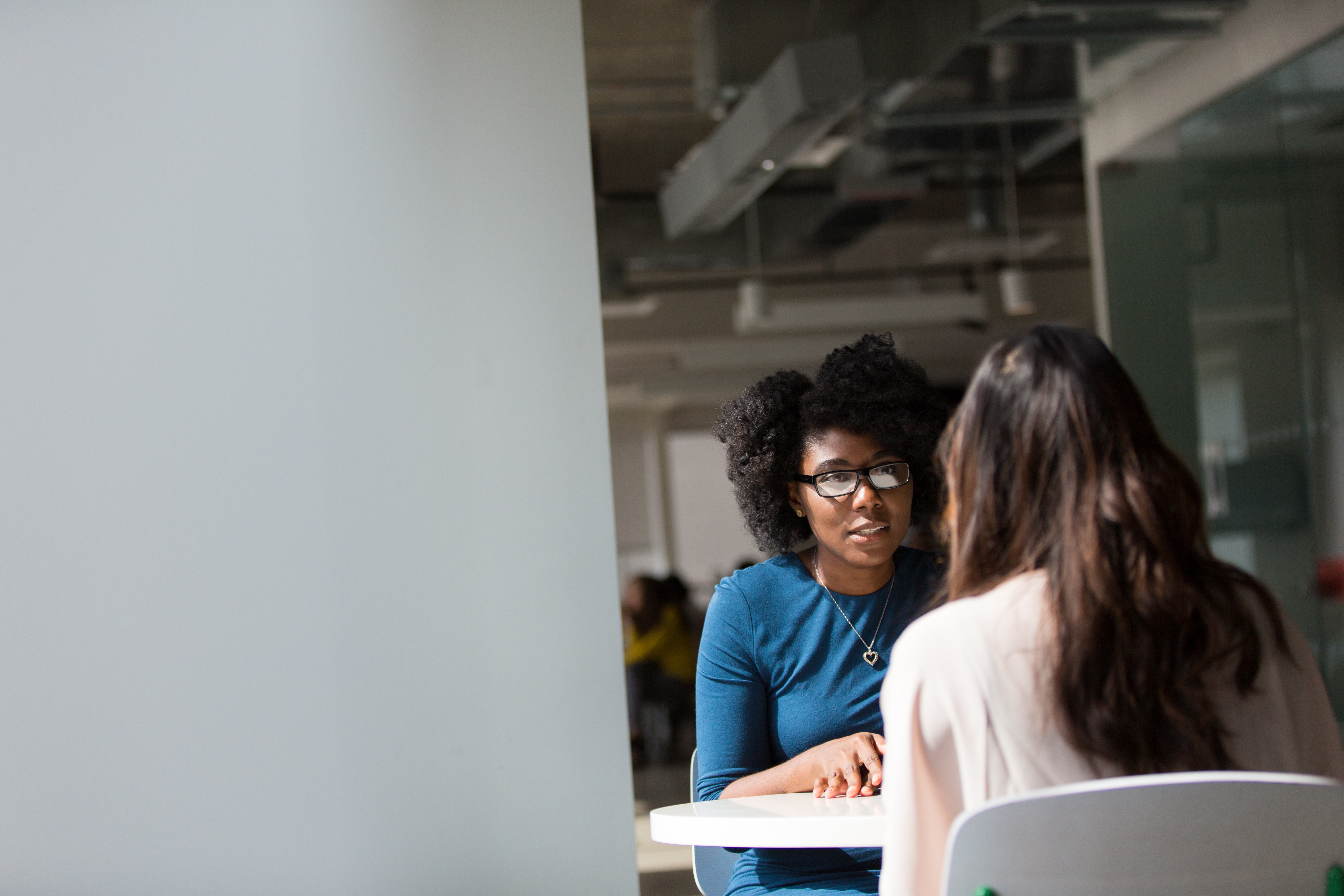 two women sitting at a small table in an open floor office